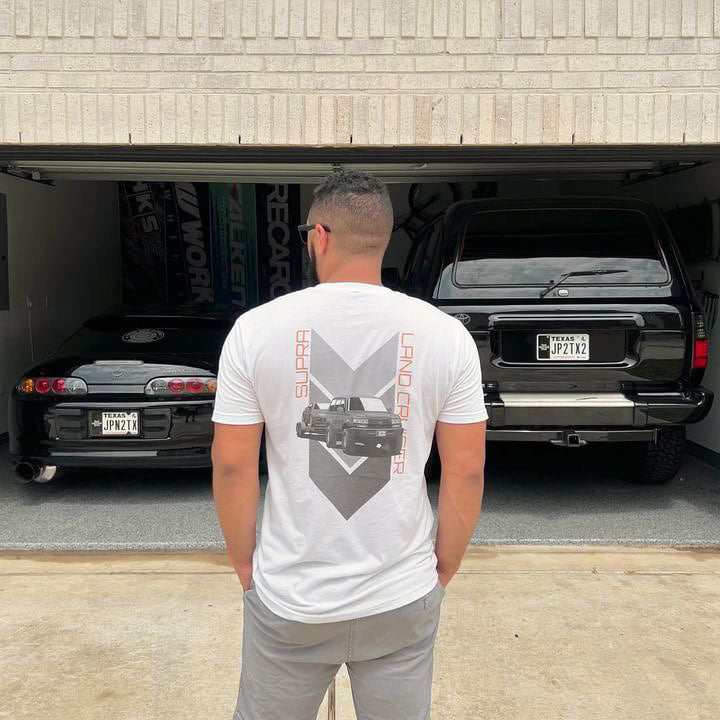 A man stands beside a 1993 toyota supra and a 90s land cruiser modeling for the shirt.