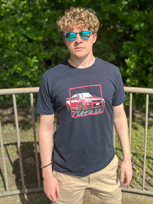 A model poses with the GTR shirt. This one features a pink r34 encircled by a box with text outlined behind it reading tuned.