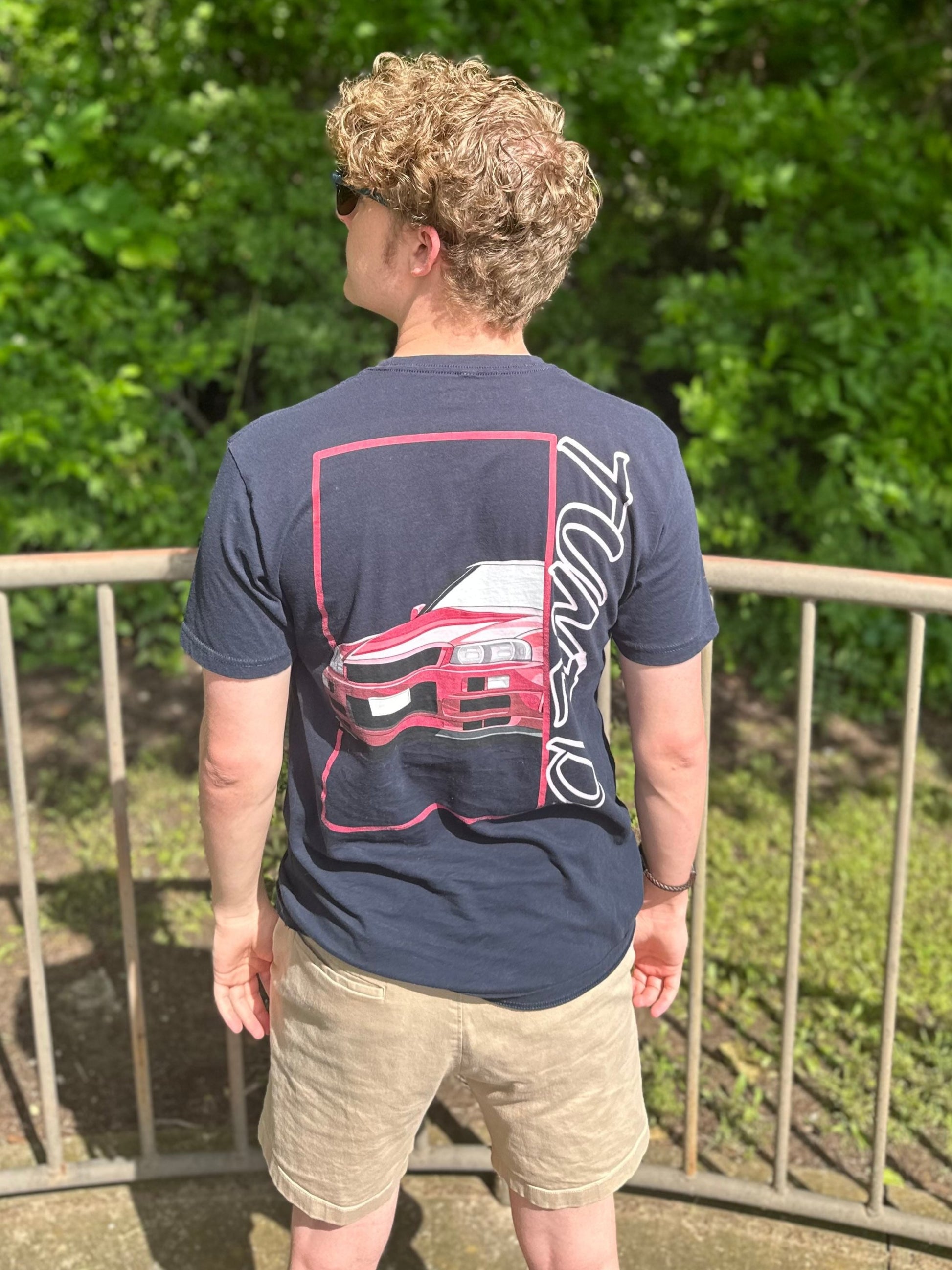 From the back, the shirt focuses on the beautiful front end of the R34 GTR. Large Text written in street style off to the side reads: T U N E D.